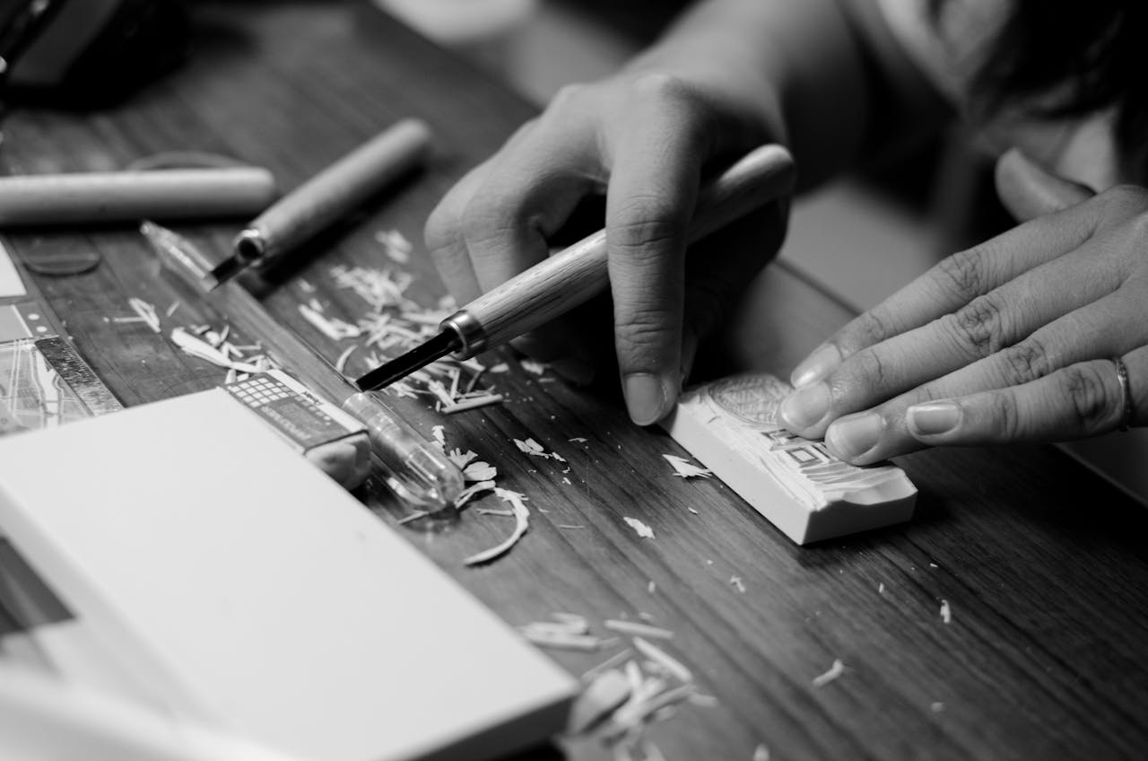 Close-up of hands carving an intricate design on a block, showcasing creativity and craftsmanship.